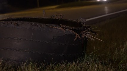 Exploded tire of semi truck on highway roadside at night. 
