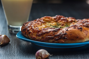 Bread with garlic and cheese and a glass of milk on a dark wooden background.