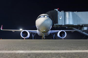 Front view of a white passenger aircraft connected to an external power supply on an airport night apron near the air bridge