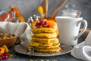 Pumpkin pancakes with honey, nuts and berries on a plate. Homemade pumpkin pancakes autumn food.  Pumpkin pancakes with maple syrup and honey on dark table. Pumpkin pastries for breakfast. 