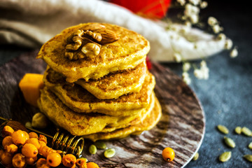Pumpkin pancakes with honey, nuts and berries on a plate. Homemade pumpkin pancakes autumn food.  Pumpkin pancakes with maple syrup and honey on dark table. Pumpkin pastries for breakfast. 