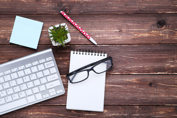 Computer keyboard with office supplies and glasses on brown wooden table