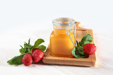 Jar of honey on a wooden board with strawberries on a white background. Still life concept. View from above.