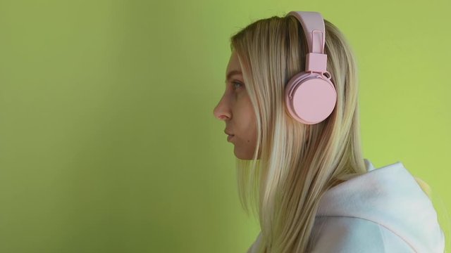Close up young caucasian girl in pink headphones in loft room with green wall listen indie hip hop lofi chillhop music at 5g