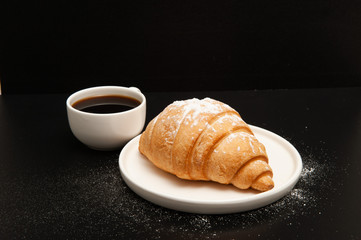 Croissant with a cup of coffee on a black background