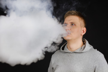 Men in hoodie vaping and releases a cloud of vapor. Selective focus