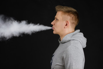 Men in hoodie vaping and releases a cloud of vapor. Selective focus