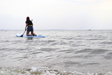Girl on sup board. Water sport, supsurfing. Active weekend at sea, woman leisure stand