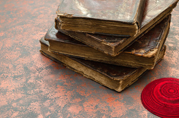 A stack of old leather-bound Jewish books with gold stamping and red knitted jewish bale