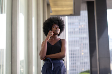 A pensive African american woman talking on a cell phone, city skyscrapers on the background