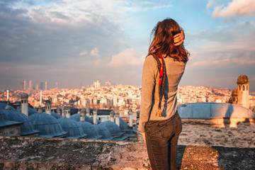 A young woman tourist from the back in full growth stands against the background of the panorama of Istanbul in the setting sun. A girl admires the panorama of the Golden Horn in Istanbul at sunset.
