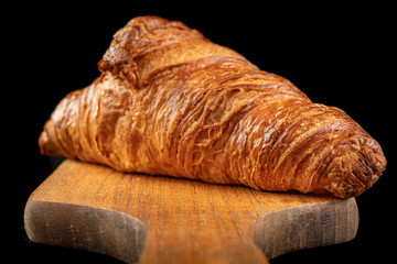 Tasty fresh croissant on a dark breadboard. Prepared bread on the kitchen table.