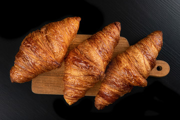 Tasty fresh croissant on a dark breadboard. Prepared bread on the kitchen table.