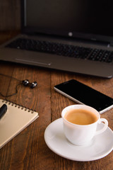 Cup of coffee on a laptop keyboard. Work place modern. Laptop (notebook) with cup of coffee and notepad with pen on old wooden table.