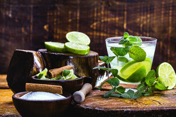 Mojito cocktail with lime, rum and mint in the tall glass on a rustic wooden table. Summer drink made in Havana.