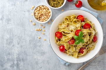 Fettuccine pasta with sauce pesto, cherry tomatoes, pine nuts and parmesan cheese on concrete...