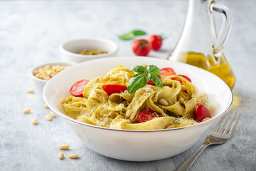Fettuccine pasta with sauce pesto, cherry tomatoes, pine nuts and parmesan cheese on concrete background. Selective focus.