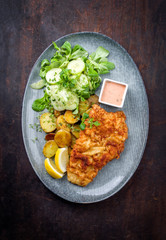 Frittiertes Wiener Schnitzel vom Kalb von der Oberschale mit Pommes und Salat als Draufsicht auf einem Modern Design Teller