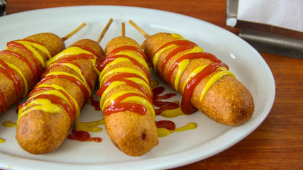 Golden corn dogs in a plate with ketchup and mustard