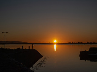 Fisherman silhouette on a pier, Sunset over ocean, Calm and peaceful atmosphere. Warm colors.