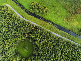 Drone top view on a park scene, Small creek and walking path, Round shape meadow in a forest.