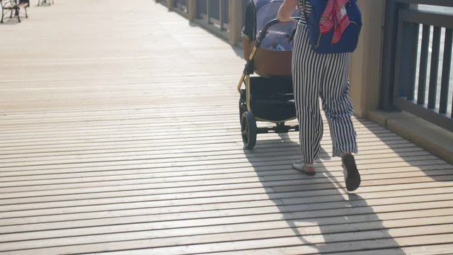 Mother walks with a pram at promenade. Family, motherhood and people concept - happy mother with baby sleeping in stroller walking at promenade summer. Medium shot.