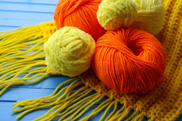 Colorful yarn balls and knitted scarf on color wooden background