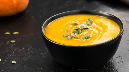 Vegetarian cream soup with pumpkin and seeds in black bowl
