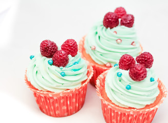 Tasty cupcakes with three large fresh raspberries on top