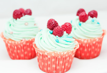 Tasty cupcakes with three large fresh raspberries on top