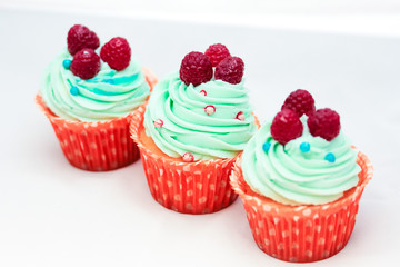 Tasty cupcakes with three large fresh raspberries on top