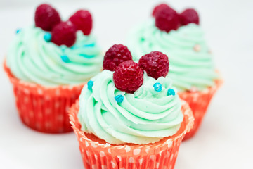 Tasty cupcakes with three large fresh raspberries on top
