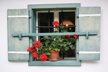 window of alpine house with wooden shutters and geranium flowers