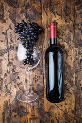 Red wine in a glass and ripe grapes on wooden background, top view