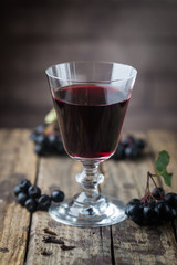 homemade black chokeberry wine or liqueur with ripe berries on wooden background