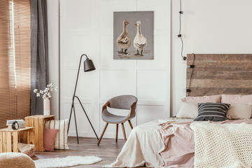 Black industrial lamp next to stylish grey wooden chair in the middle of delightful bedroom interior
