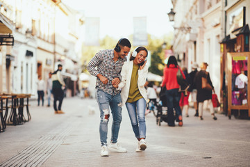 Happy young couple dancing on the street and listening to music through headphones