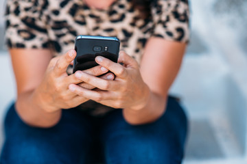 Close-up image of young girl sitting at home interior and using modern smartphone device, female hands typing text message via cellphone, social networking concept