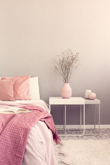 Dry flowers in pastel pink vase on simple nightstand table next to bed