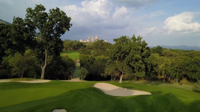 golf course in a forest of ash with the historic monastery of escorial crowning a hill, aerial view over a golf fairway