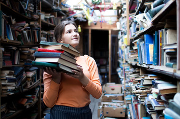 girl student holds a stack of books in the library, she searches for literature and offers to read, a woman prepares for study, knowledge is power, concept bookseller