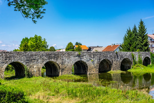 Old stone bridge (Marmont bridge) on river Zagorska Mreznica, near Ogulin, Croatia, red roofs and blue sky, sunny summer day