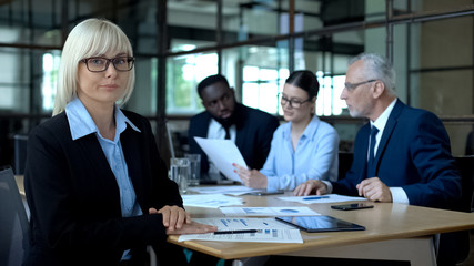 Female financial analyst looking camera, business partners working background