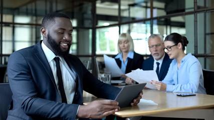 Smiling black businessman reading tablet report, satisfied successful project