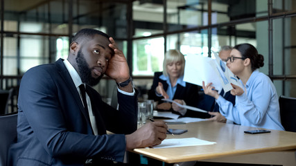 Male company employee feeling tired listening to shouting colleagues in office
