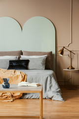 Golden lamp on modern nightstand table next to blue bed in grey bedroom interior