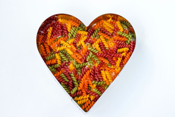 Fusilli multicolored pasta heart shaped on a white background, horizontal orientation, top view