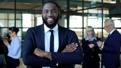 Fototapeta premium Smiling african businessman with folded arms, office work, corporate success