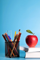  School supplies pencils, pens, ruler, brush , books, eyeglasses and apple on a blue background with a place for text