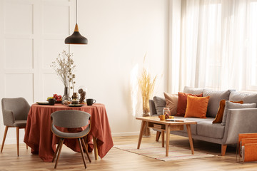 Living and dining room interior with grey couch and table covered with orange tablecloth